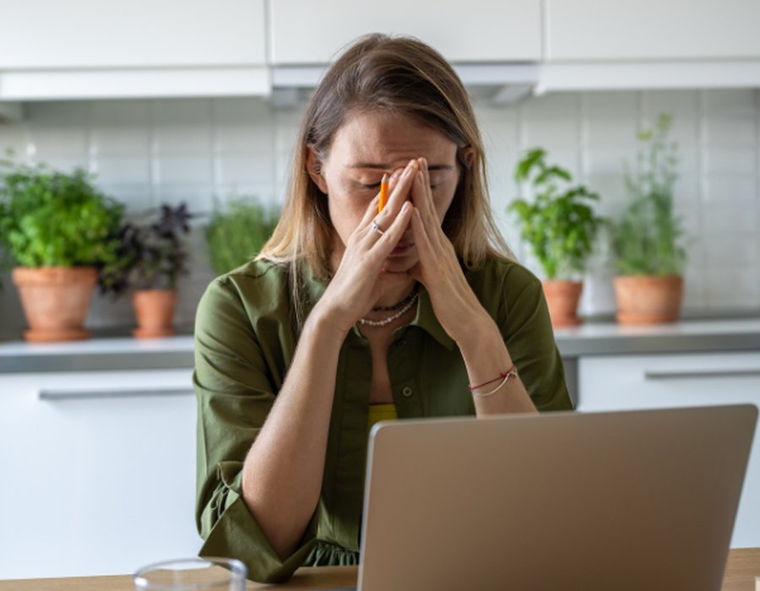 A woman pausing at a laptop with her hands over her face